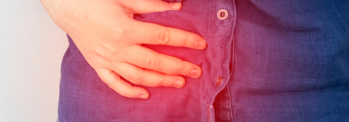 A woman in a denim shirt holding her tummy in pain