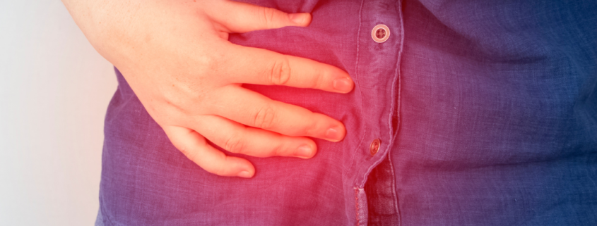 A woman in a denim shirt holding her tummy in pain