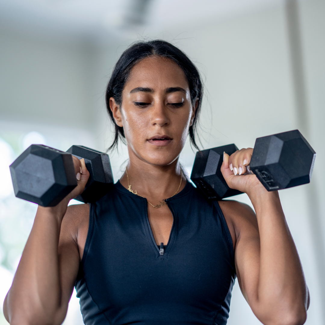 A woman looking down as she holds two dumbbells at her shoulders