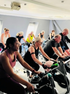 Two rows of diverse people exercising on spin bikes.