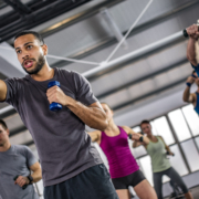 Men and women exercising with dumbbells in gym.