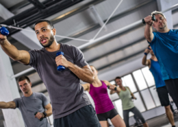 Men and women exercising with dumbbells in gym.