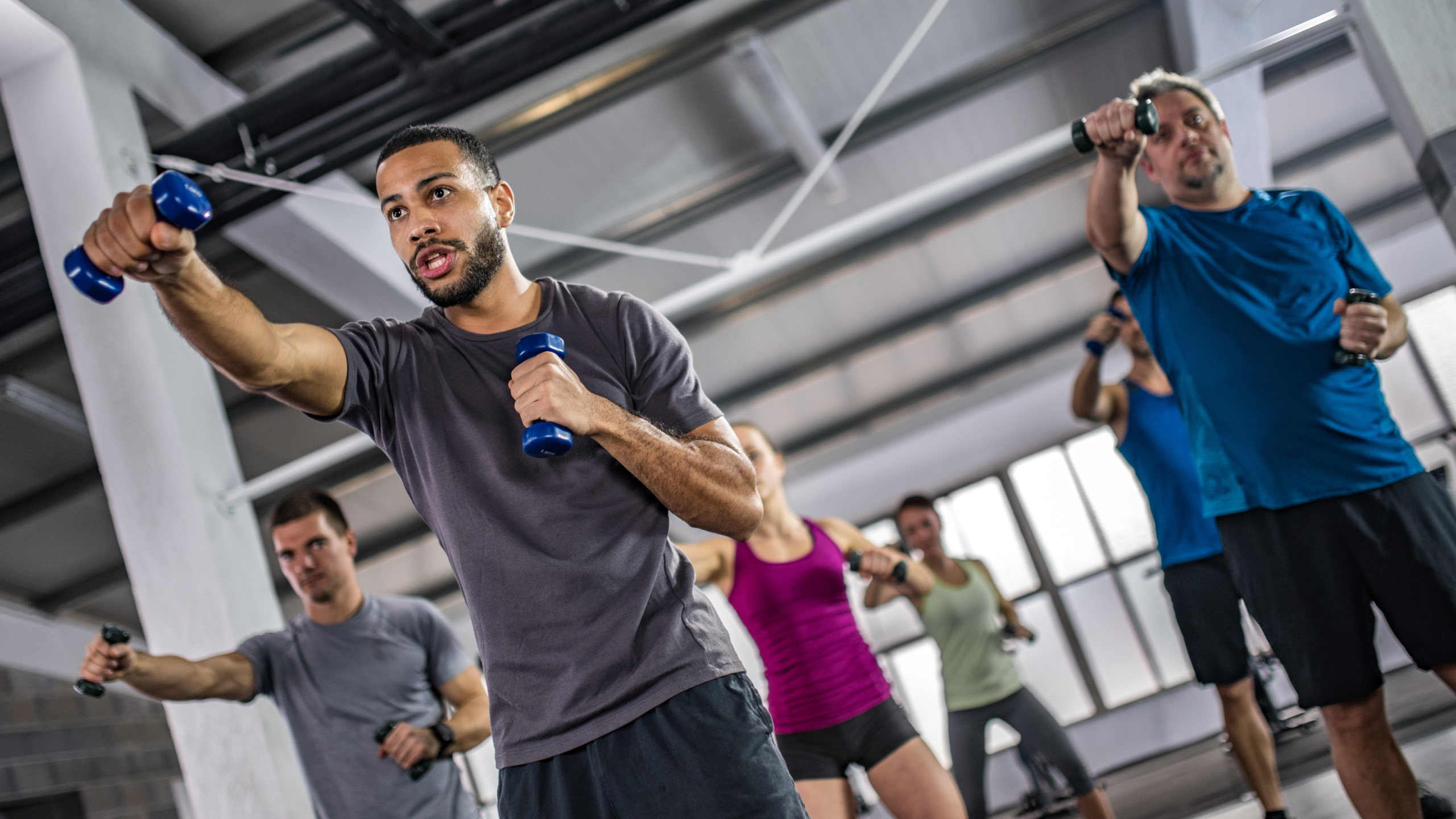 Men and women exercising with dumbbells in gym.